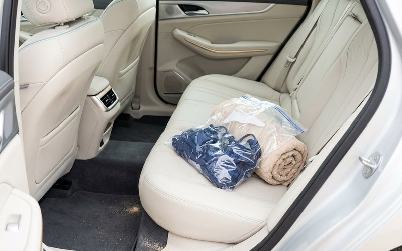 濡れた水着やタオルをビニール袋に入れて車のシートに置いた様子(足元に砂)
