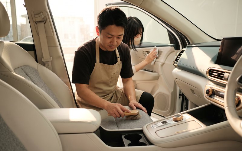 長久手市の西村コーティングで、軽自動車の本革シートに残った土汚れを乗降側の角から確認しながら洗浄している場面