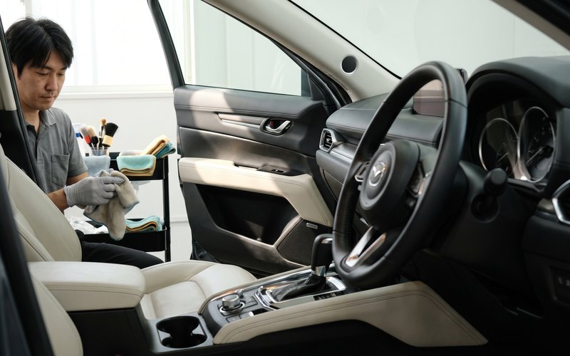 運転席の足元とシート横に残った液だれの跡を専用機材で洗浄している作業の様子