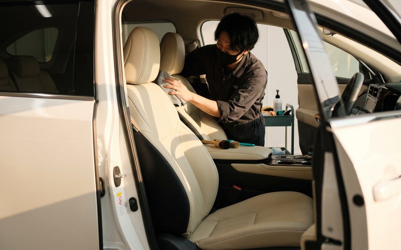得洗隊 株式会社での作業カット。本革シートのシボとステッチ部分に入り込んだ汁の跡を、専用の道具で丁寧に取り除いているところ
