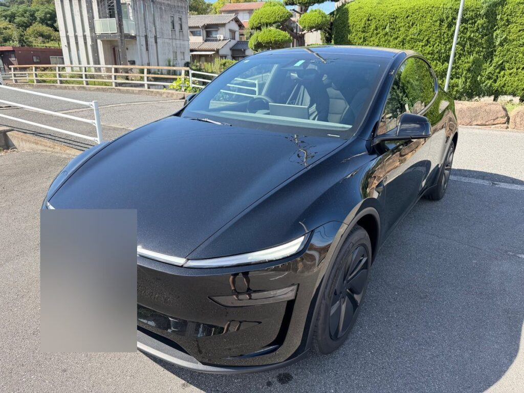 晴れた日に屋外で撮影した黒のテスラ モデルY（ナンバーはぼかしています）